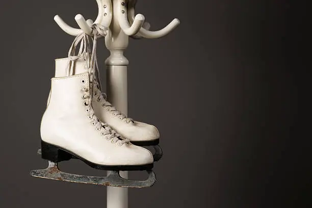 Figure skates hanging frm a bent wood hatstand on a grey background.