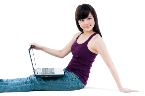 Portrait of an attractive young Asian woman sitting on floor with laptop over white background.