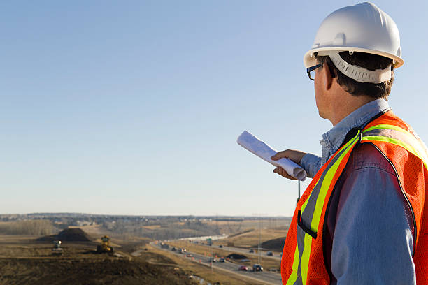Survey "A royalty free image from the construction industry of an architect as he surveys a construction site, plans in hand." civil servant stock pictures, royalty-free photos & images