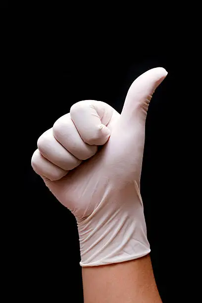 Doctor's hand with a surgical glove showing the OK sign(giving thumbs up) isolated on black background.