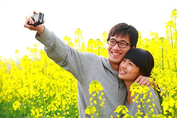 young asian couple taking picture of themselves in the rape field 