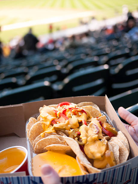 Nachos at a Baseball Game Ballpark Sports Stadium A person's hands holding a box of nacho chips at a baseball ballpark. baseball stadium chairs stock pictures, royalty-free photos & images