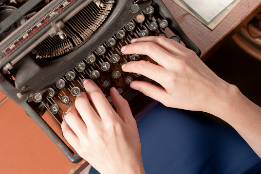 A man types on an antique typewriter in an office.  Click to view similar images.