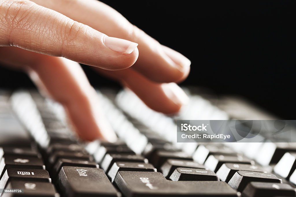 Woman's hands type on computer keyboard against black "A young woman's hands type on a computer keyboard, against a black, nighttime background." Adult Stock Photo
