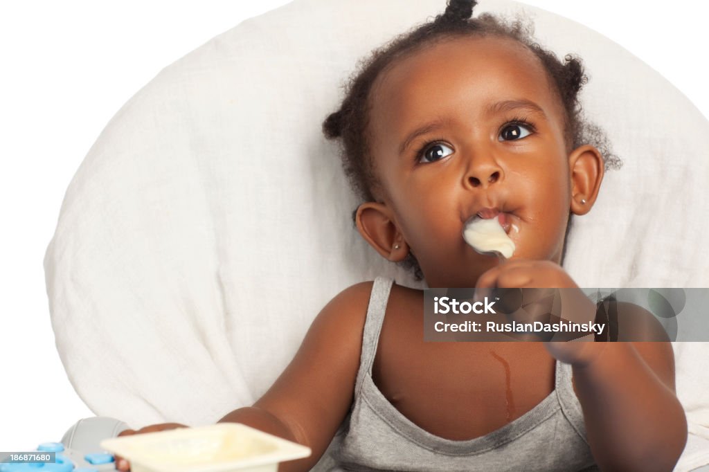 Baby girl eating with spoon. Close up portrait of baby girl eating yogurt. Eating Stock Photo