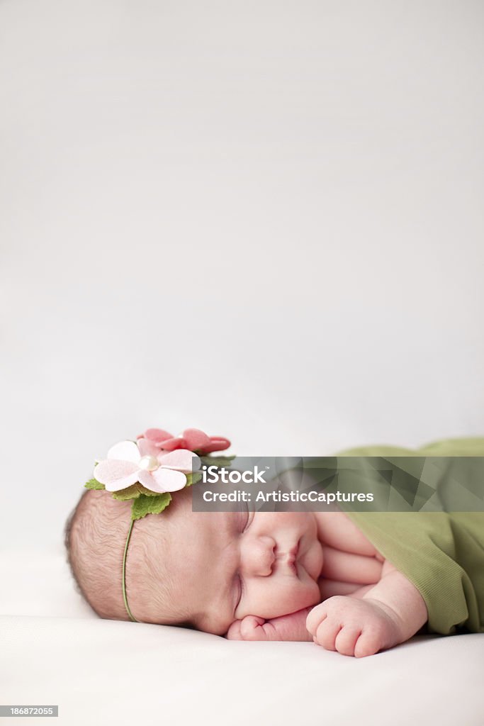 Newborn Baby Girl Swaddled in Soft, Green Blanket "Color image of a newborn baby girl wearing flowered headband and sleeping peacefully while swaddled in a soft, green blanket. Image is on white background with copy space." 0-1 Months Stock Photo