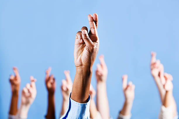 istock Fingers crossed for luck, many hands raised against blue sky 186873589
