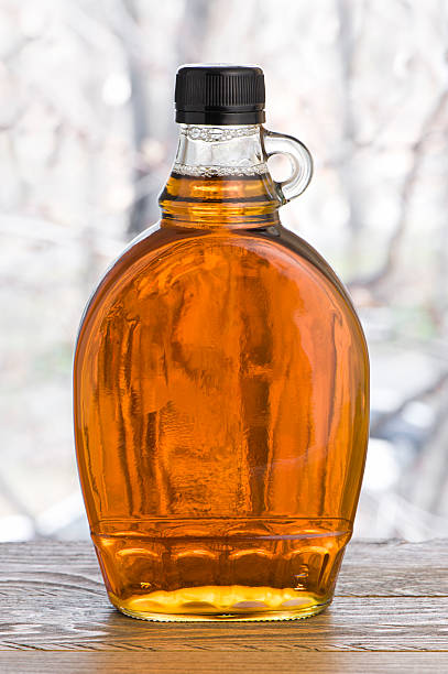 Maple syrup "Bottle of maple syrup on a wooden shelf, with maple trees out of focus in background. More maple syrup..." maple syrup stock pictures, royalty-free photos & images