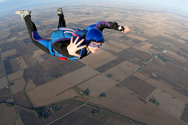 Young lady skydiving whilst mid-air waving to camera A young woman smiles and looks relaxed in freefall. skydiving stock pictures, royalty-free photos & images