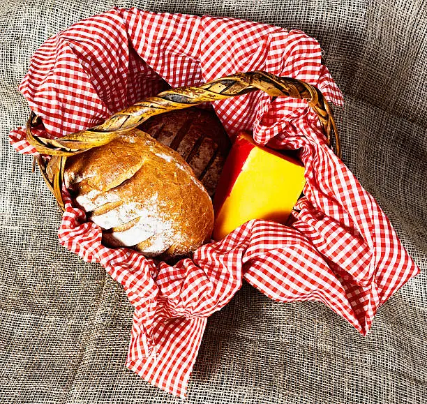 All ready for a home-made Ploughman's Lunch or healthy cheese sandwich: cheese and rustic bread in a gingham-lined basket on hessian.