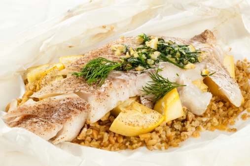 Two haddock fillets with freekeh, yellow squash, lemon. butter and dill. Preparing to cook in parchment paper.