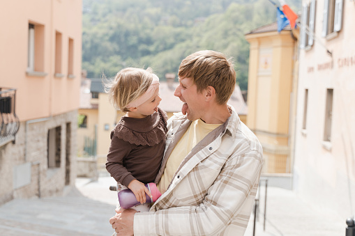 Father and little daughter stick their tongue out at each other in San Pellegrino Terme, Lombardy, Italy
