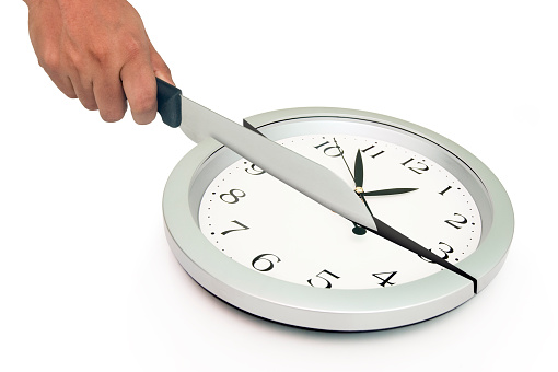 Wall clock being cut in half by a knife isolated on white background.