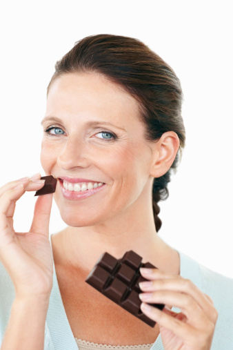 Closeup of a smiling Caucasian woman eating a chocolate against white