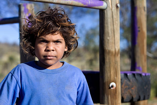 Aboriginal child standing against wooden playground stock photo