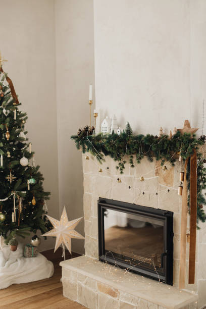 istock Stylish decorated fireplace mantel with christmas branches, decorations and bells on background of modern christmas tree with lights. Rustic christmas living room in modern farmhouse 1868877560