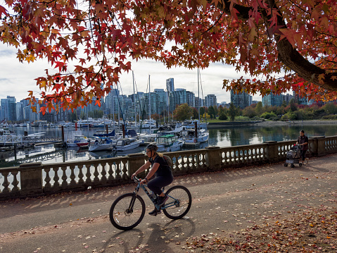Woman cycling at Stanley Park on a sunny autumn afternoon. Royal Vancouver Yacht Club in the background.