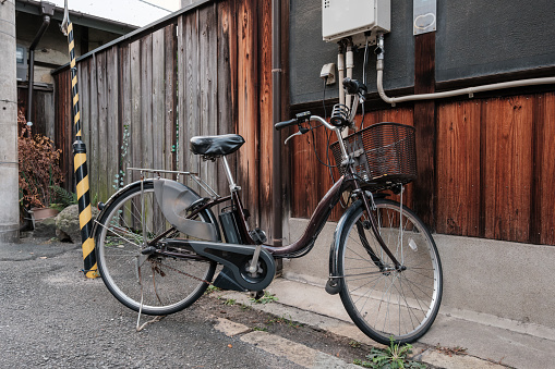 Black bicycle with metal basket parked beside an old wooden wall.