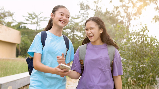 Happy Asian student girls walking and using smart phone in school