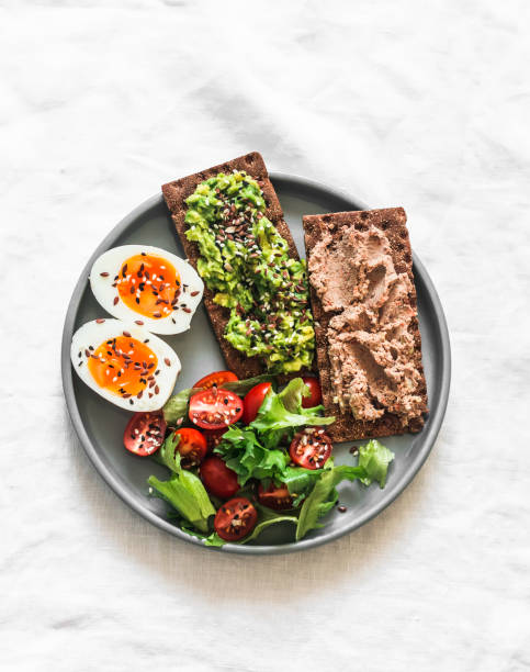 Delicious breakfast, tapas, snack - crispy rye bread crackers with turkey liver, avocado, boiled egg and cherry tomatoes on a light background, top view Delicious breakfast, tapas, snack - crispy rye bread crackers with turkey liver, avocado, boiled egg and cherry tomatoes on a light background, top view egg cherry tomato rye stock pictures, royalty-free photos & images