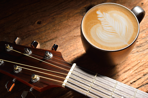 A cup of cafe latte and guitar on wooden table.