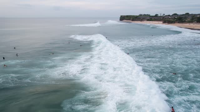Wave appears quickly and surfers try to catch it, some succeed, aerial arc shot