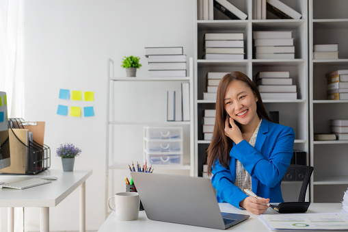 Asian female employee is talking on the phone with client, partner, commercial consultant at table in office with copy space background.