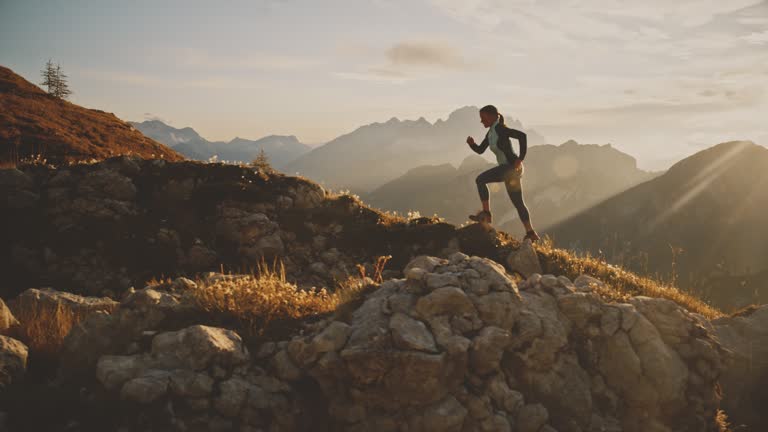 Woman jogging up grassy hill in sunny,majestic morning mountains