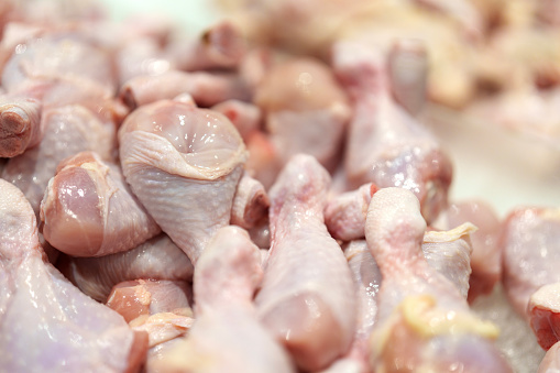 A pile of raw chicken drumsticks is on display at a market stall, ready for sale.