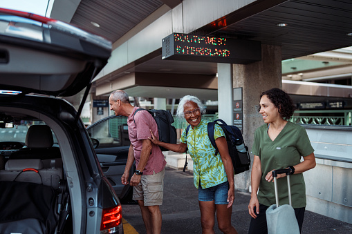 A vibrant multiracial woman of Hawaiian and Chinese descent who just arrived in Hawaii with her Caucasian husband smiles with excitement as she greets family outside the airport.