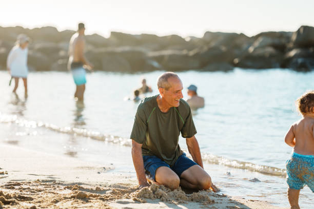 istock Senior man sits on sandy beach playing with grandson 1869117352