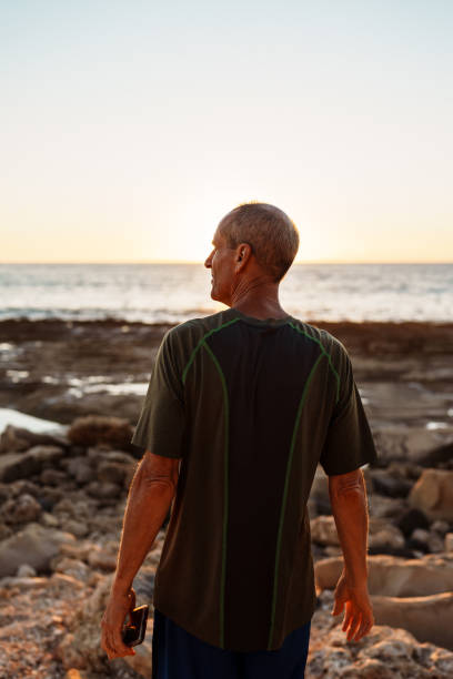 istock Man walks on rocky beach shore during sunset 1869117873