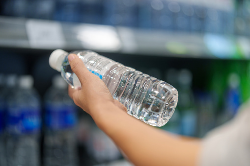 Close up woman's hand woman selecting a bottle of water from the shelf in a grocery store