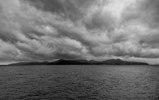 A grayscale shot of silhouettes of hills and a lake under the sky with dark clouds - depression concept