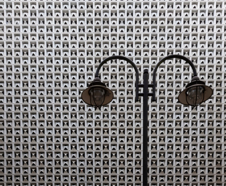 The distinctive wall cladding found on many department stores in Germany, installed in the 1980s. Repetitive pattern from wall with street lamp in the front. This is in fact, a colour photo.