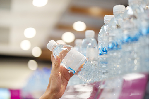 Close up woman's hand woman selecting a bottle of water from the shelf in a grocery store