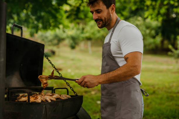 Caucasian man happily tending to the barbecue in his homey backyard