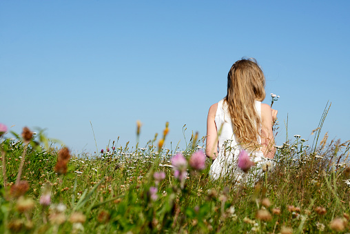 Girl between wildflowers on a meadow, smelling on a flower. Selective focus, rear view and copy space.  Taken in Friesland, German North Sea Region, Lower Saxony, Germany, Europe