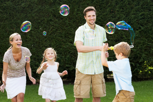 Family Playing With Bubbles In Garden Smiling To Camera