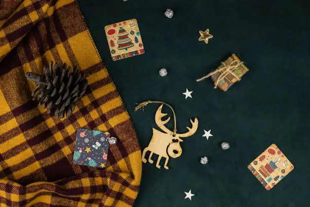 Christmas and New Year background, giftcards, wooden deer, pine cone on dark green and yellow woolen plaid