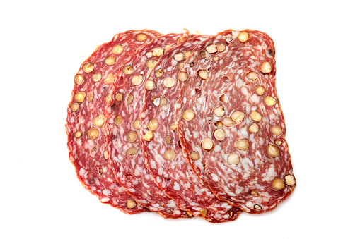Sliced dry sausage with hazelnut in front of white background