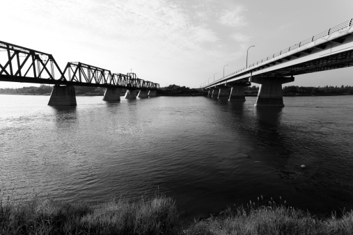 The Diefenbaker Bridge and old train bridge over the North Saskatchewan River in Prince Albert, Saskatchewan. Processed in black and white.