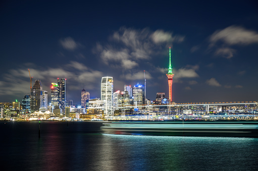 Sky Tower lit up in red and green for Christmas. Long exposure with light trails of a boat sailing past Waitemata harbour. Auckland.