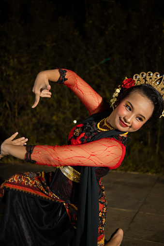 an Asian dancer dancing on her knees while wearing a black and luxurious costume in front of the audience at night