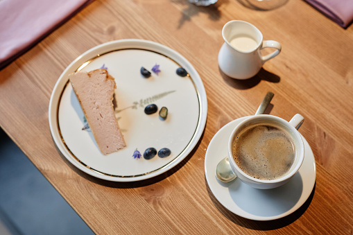 Above angle of wooden table in restaurant or cafe with cup of aromatic cappuccino and plate with piece of fresh tasty cheesecake