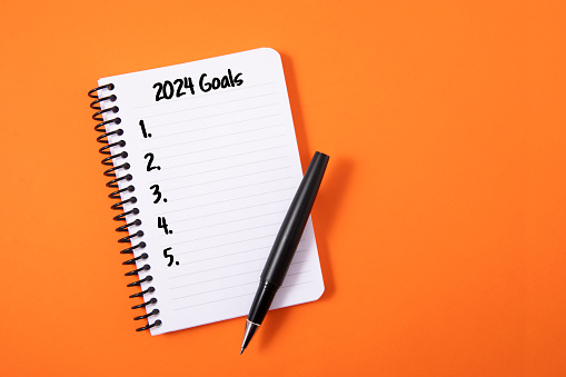 2024 goals in note pad on orange colored background