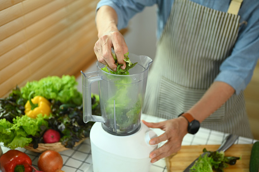 Healthy senior man in apron preparing vegan organic smoothie on kitchen