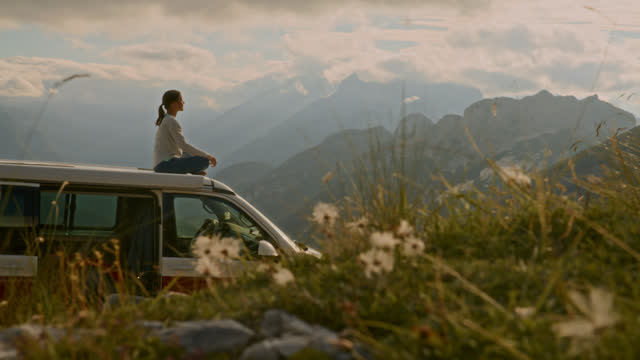 SLO MO Serene Woman Meditating on Top of Van in Remote ,Majestic Mountains. A Woman Enjoys a Beautiful Mountain View.