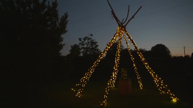 A glowing huge teepee in the evening in the backyard next to the trees