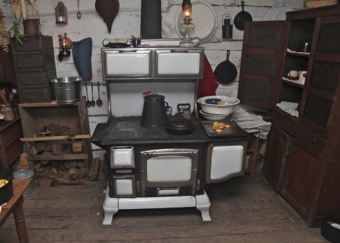 A pioneer kitchen with a wood burning cook stove, kerosene lamps,  and fresh baked biscuits.  There are also two flat irons heating on the stovetop, and a stovetop toaster heated up, and ready for bread.  This was at Pioneers Days in Fowler Park, Vigo County, Indiana.